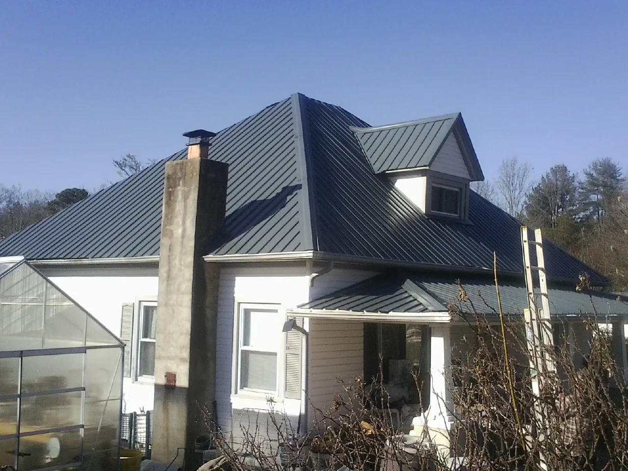 Dark blue standing seam metal roof on a white farmhouse with dormer — Slate & Tile Roof Repair by Roofing Brothers in Lanett