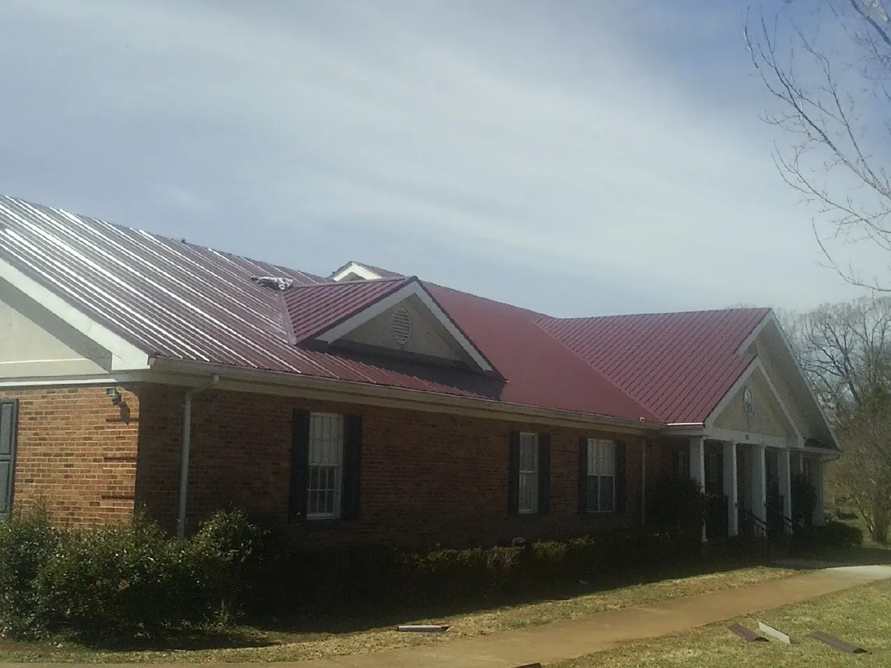 Red metal roof with gabled entries on a long brick building, from a Hail Damage Roof Repair job in Lanett
