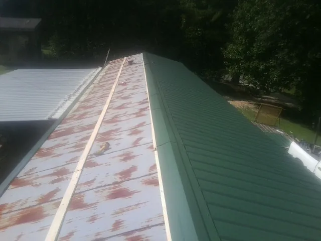 Old rusted panels beside newly installed green metal roofing — Wind Damage Roof Repair by Roofing Brothers in Lanett