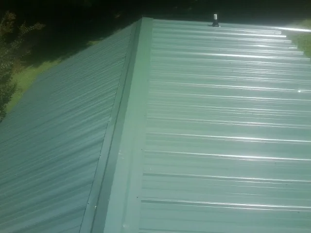 New green metal panels meeting at the ridge of a roof — Flat Roof Repair work by our crew in Lanett