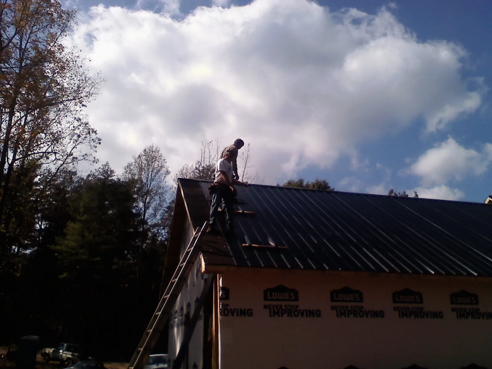 Roofer fastening dark metal panels high against a cloudy sky, from a Roof Inspection job in Lanett