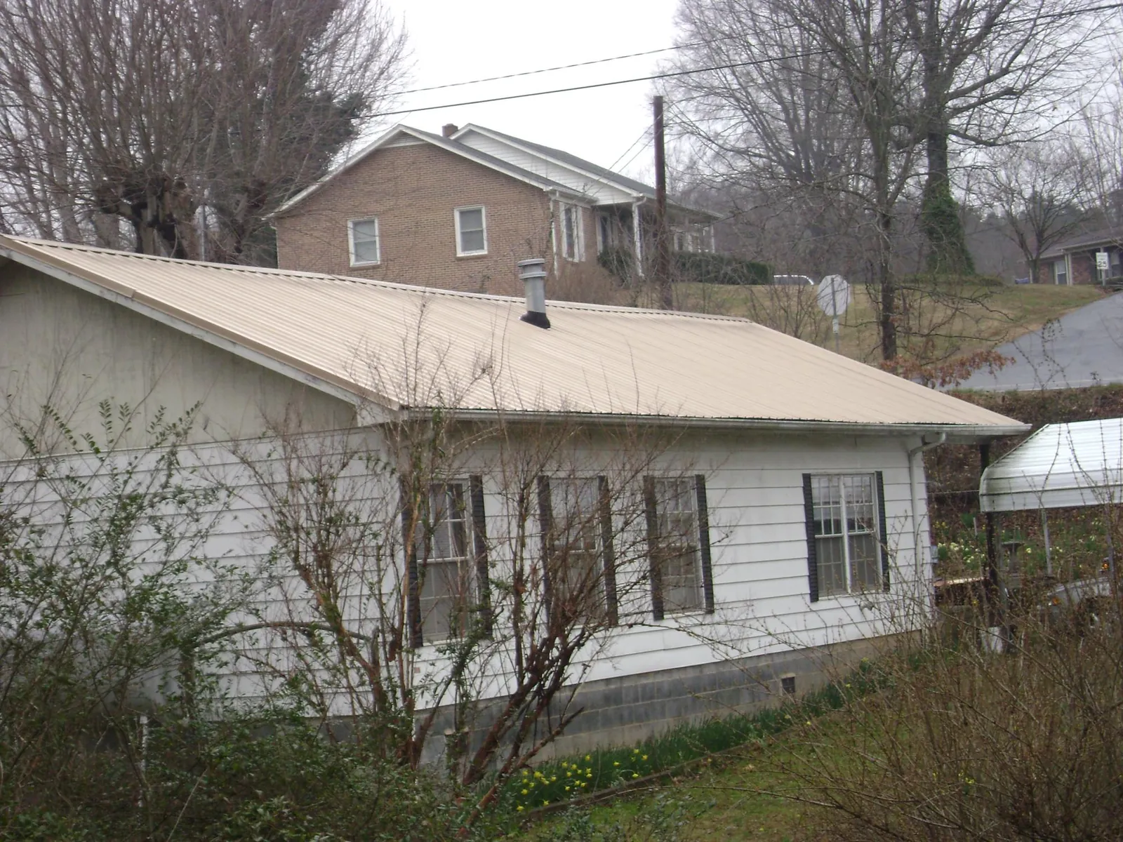 Tan metal roof on a white sided house set into a hillside — Commercial Roofing by Roofing Brothers in Lanett