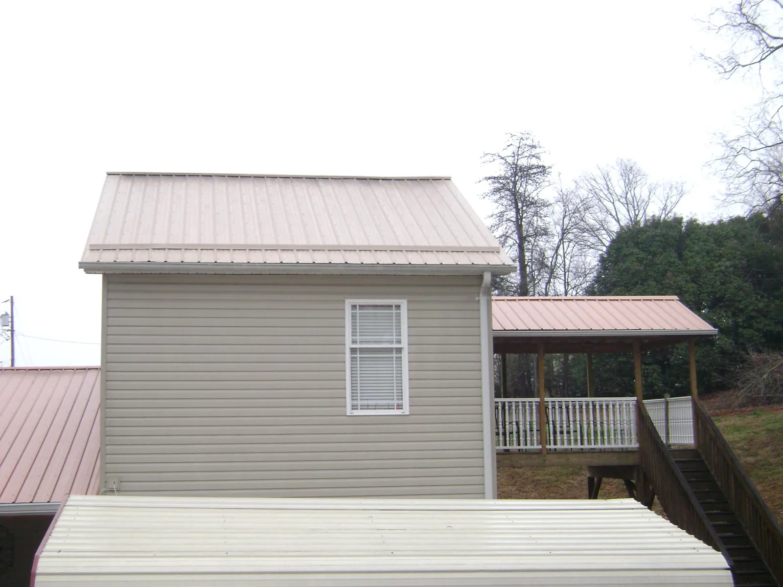 Tan metal roofs on a two story addition and attached porch, from a Roof Replacement job in Lanett